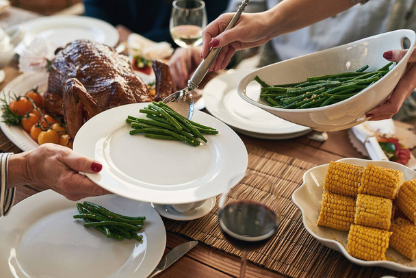 Hände, Essen und Familie an einem Tisch zum Danken, Essen und Verbundenheit im Urlaub, gemeinsames Essen zu Hause. Hand, Gemüse und Gastgeberin servieren Frau beim Mittagessen, Schlemmen und Sammeln. - Foto, Bild