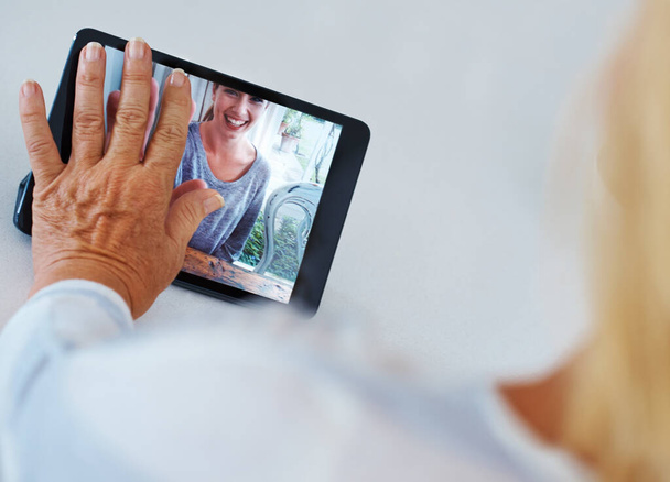 Distancia soportable. Retrospectiva de una mujer mayor tocando su tableta digital mientras tiene una videoconferencia con su nieto - Foto, imagen