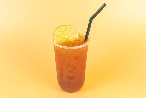 Koude thee of zwarte thee met citroen in een plastic bril op oranje achtergrond.Verfrissend drankje om af te koelen in de zomer. - Foto, afbeelding