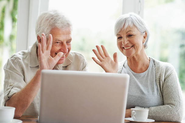 Une nouvelle technologie signifie que la famille n'est jamais loin... Un couple de personnes âgées joyeux ayant un chat vidéo sur un ordinateur portable - Photo, image