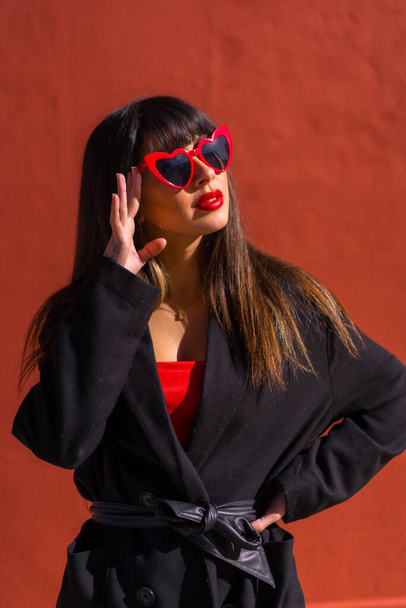 Brunette girl in a portrait on a red background with hearts glasses, Valentine's Day, fashion pose - Foto, immagini