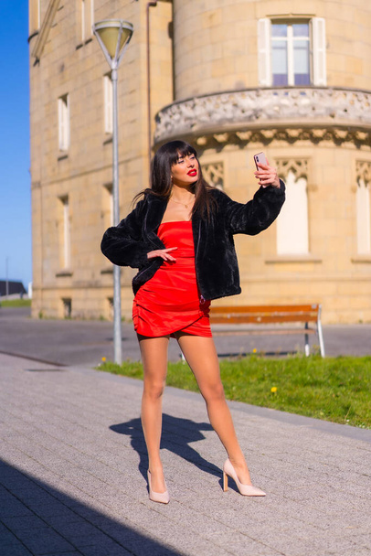 Mujer joven con vestido rojo en un hermoso castillo, tomando una selfie con sonrisa con el teléfono - Foto, imagen