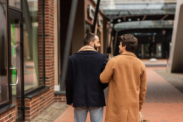 vista trasera de feliz pareja gay con bolsas de compras caminando en la ciudad - Foto, imagen