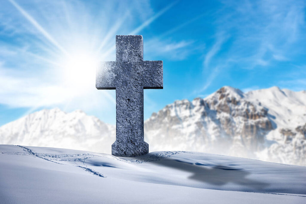 Large stone religious cross in a mountain landscape with snow against a clear blue sky with clouds, sun rays and copy space. - Photo, Image
