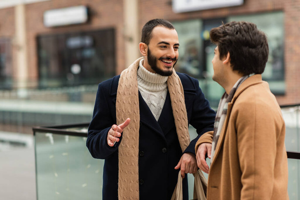 cheerful bearded gay man in trendy clothes talking to boyfriend on city street - Fotó, kép