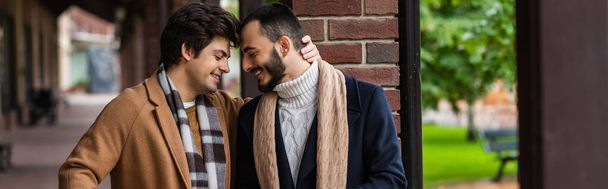 smiling gay couple in trendy coats and scarfs standing face to face with closed eyes outdoors, banner - Foto, Imagem