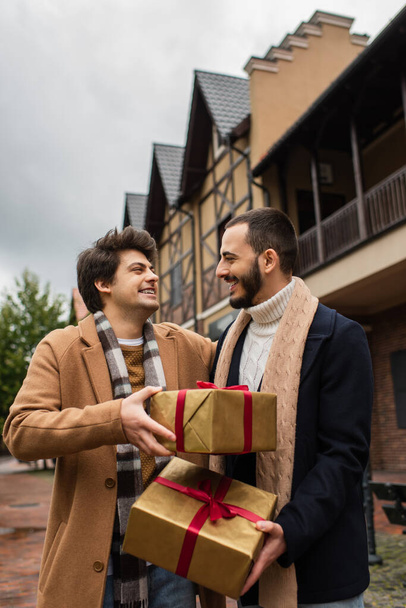happy gay couple in stylish clothes holding Christmas presents on city street - Фото, зображення