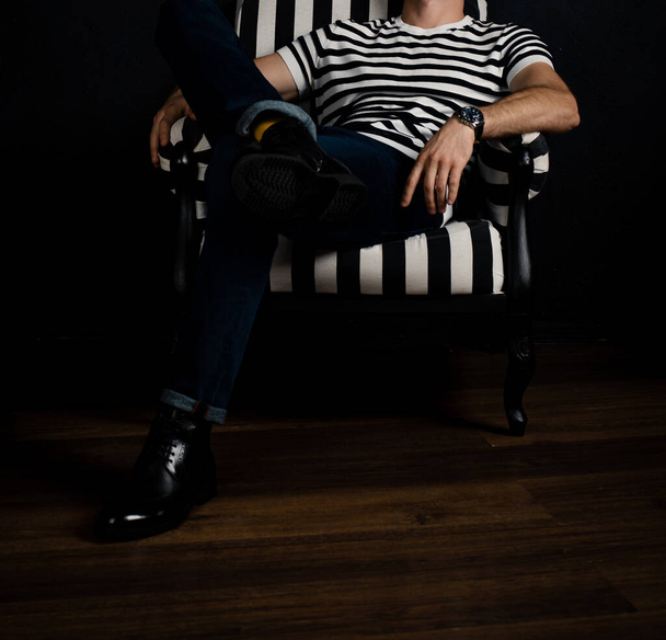 An unrecognizable man in a striped T-shirt sits on a striped armchair. - Φωτογραφία, εικόνα