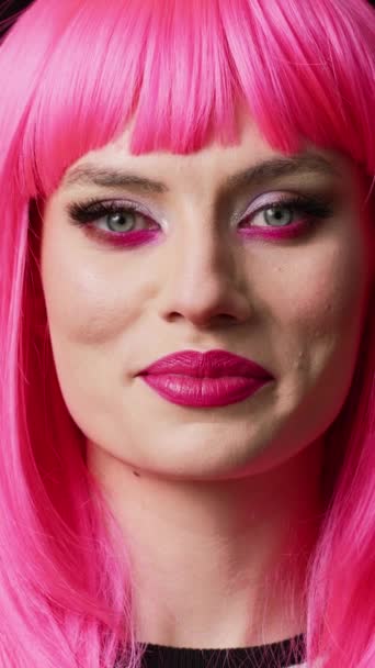 Függőleges videó: Szexi gyönyörű nő mutatja kandi mosoly a kamera, érzés boldog és pozitív. Női modell mosolygós és visel gyönyörű smink rózsaszín haj paróka, hogy vidám és magabiztos. - Felvétel, videó