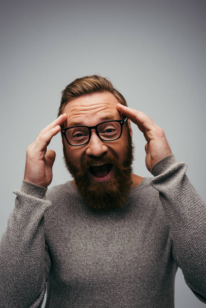 Excited and bearded man in eyeglasses looking at camera isolated on grey  - Fotografie, Obrázek