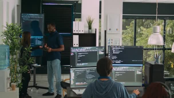 Diverse team of software engineers analyzing code on wall screen tv, using digital tablet and working with artficial intelligence. Coders parsing cloud computing project with big data. - Footage, Video