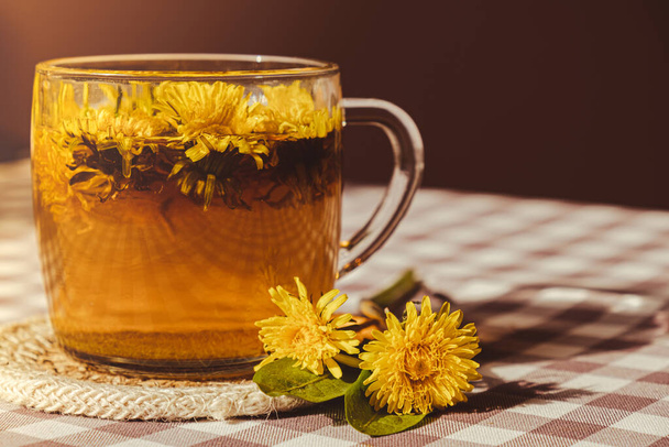 Dandelion flower healthy tea in glass cup on table. Herbal medicine Delicious tisane tea from with fresh yellow blossom dandelion flowers inside tea cup. Green clearing infusion Wildflowers Eco - Foto, Imagen