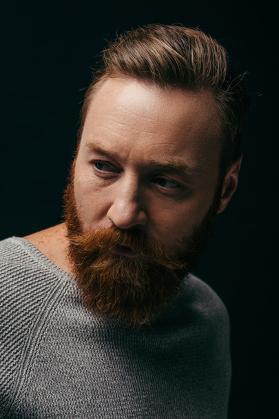 Portrait of bearded man in grey jumper looking away isolated on black  - Foto, immagini