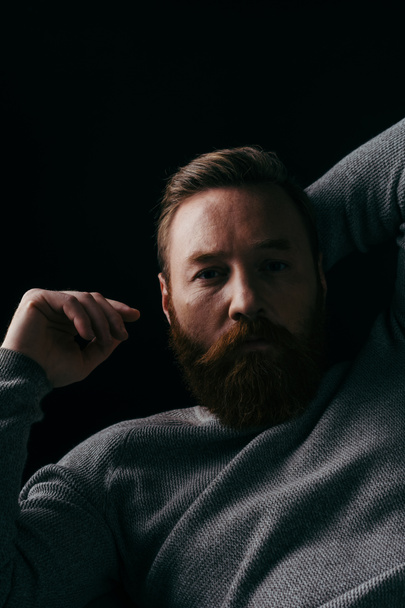 Portrait of bearded man in grey long sleeve posing in light isolated on black  - Photo, Image