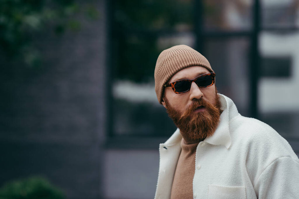 bearded hipster in stylish sunglasses and white shirt jacket looking away  - Фото, изображение
