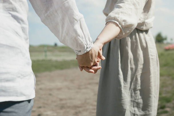 Close up couple concept photo. Holding hands. Romantic gesture. Side view photography with rural meadow on background. High quality picture for wallpaper, travel blog, magazine, article - Φωτογραφία, εικόνα