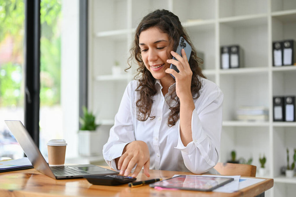 Profesjonalna, milenijna, kaukaska bizneswoman lub kobieta zajmująca się biznesem przez telefon ze swoim partnerem biznesowym podczas pracy w biurze. - Zdjęcie, obraz