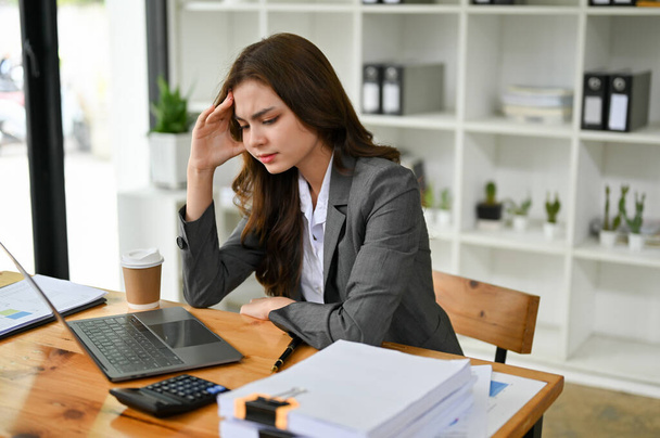 Stressed and thoughtful young Caucasian businesswoman at her desk feeling upset and dissatisfied with the results of her business project, suffering from headache or overworked. - Photo, Image