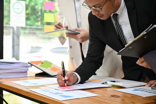 Профессиональный взрослый азиатский бизнесмен или генеральный директор мужчина проверяет и рассматривает финансовый отчет на встрече со своей командой. крупным планом и обрезанным изображением - Фото, изображение