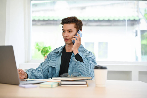 Jeune asiatique intelligent et professionnel employé de bureau contact avec son client au téléphone, parler au téléphone tout en travaillant à son bureau. - Photo, image