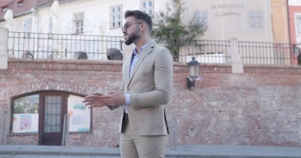 wideo projektowe eleganckiego biznesmena mody pocierającego dłonie, układającego okulary przeciwsłoneczne, rozglądającego się i odchodzącego z ręką w kieszeni - Materiał filmowy, wideo