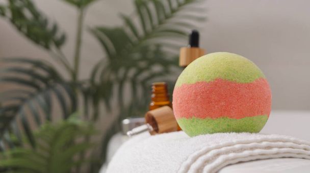 Towel with bath bomb and bottles of essential oils on tub indoors, closeup. Space for text - Zdjęcie, obraz