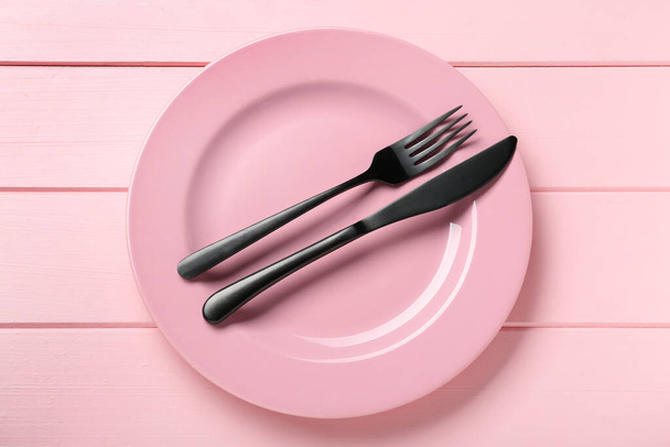 Ceramic plate with cutlery on pink wooden table, top view - Φωτογραφία, εικόνα