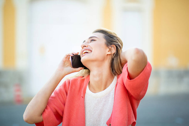 Όμορφη γυναίκα διασκεδάζει μιλώντας στο κινητό τηλέφωνο με τα χέρια της πίσω από το κεφάλι - Φωτογραφία, εικόνα