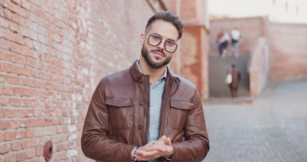 confident man pulling and adjusting leather jacket, rubbing palms, looking cool, crossing arms, smiling and touching beard while looking to side outdoor in an old city - Footage, Video