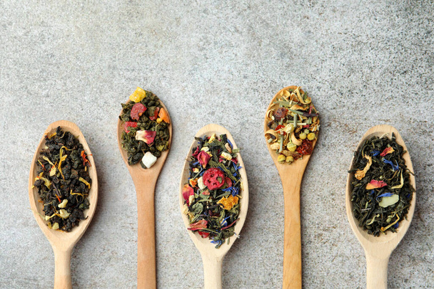 Different kinds of dry herbal tea in wooden spoons on light grey table, flat lay - Foto, immagini