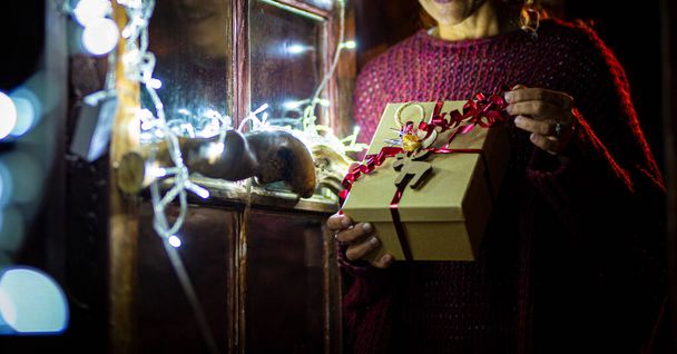 Közelíts banner képet a karácsonyi ajándékok ajándék megosztása. Egy nő kipakolja a bürokráciás dobozt karácsony estére. A decemberi ünnepeket otthon ünnepeljük. Fények az előtérben. Meglepetés ajándék átvétele - Fotó, kép
