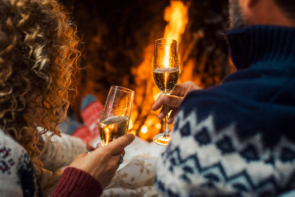 Powrót widok pary korzystających i świętujących razem brzęczenie z flet szampana wewnątrz domu z kominkiem w tle. Zimowy sezon wakacyjny i miłość w związku. Rocznica nowego roku - Zdjęcie, obraz