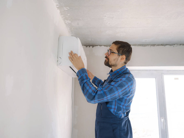 νεαρός άνδρας με μπλε κοστούμι κάνει επισκευή διαμέρισμα. Σχέδιο ανακαίνισης σπιτιού. Ρύθμιση τύπου συστήματος κλιματισμού - Φωτογραφία, εικόνα