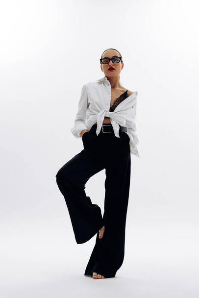 Young woman in glasses poses in pants and shirt against white background. - Φωτογραφία, εικόνα