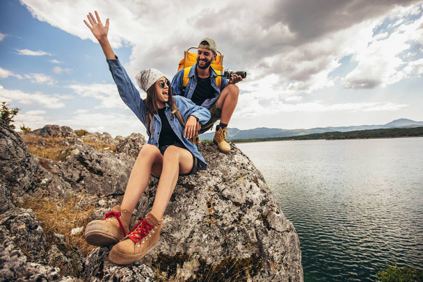 Turyści z plecakami siedzący na klifie i cieszący się górskim jeziorem - Zdjęcie, obraz