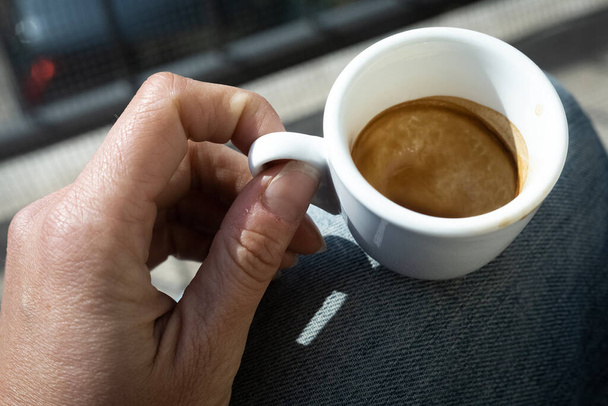 Menschliche Hand mit kleiner weißer leerer Tasse Espresso-Kaffee im hellen Sonnenlicht. Moment der Meditation. Kaffeebremse vorhanden. . Hochwertiges Foto - Foto, Bild
