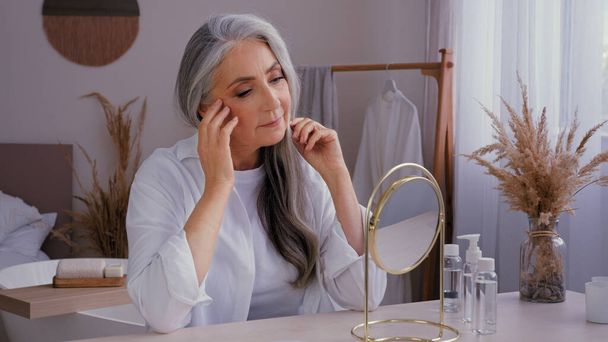 Běloch 60s ve věku senior starší dáma starý šedovlasý 50s žena žena dívá na zrcadlo odraz hýčkání dotýkání vrásčitý obličej anti-aging chirurgie zvedání vrásky obličeje péče o pleť hydratační - Fotografie, Obrázek