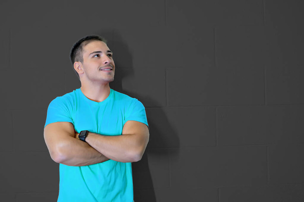 Nice picture with young caucasian male athlete crossing his arms smiling and looking to the side. Confident and positive success concept. Goal achievement. Blank wall, copy space. - Photo, Image