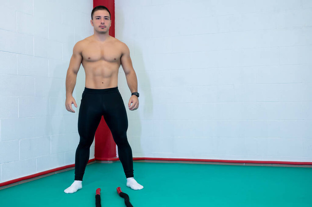 Nice picture with charming young shirtless Caucasian male athlete posing in front of battle ropes. Look into camera. Confident and positive success concept. Goal achievement. Copy space. - Photo, Image