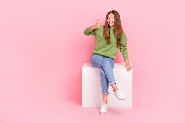 Full length photo of charming cute schoolgirl wear green sweatshirt sitting white chair thumb up empty space isolated pink color background. - Fotoğraf, Görsel