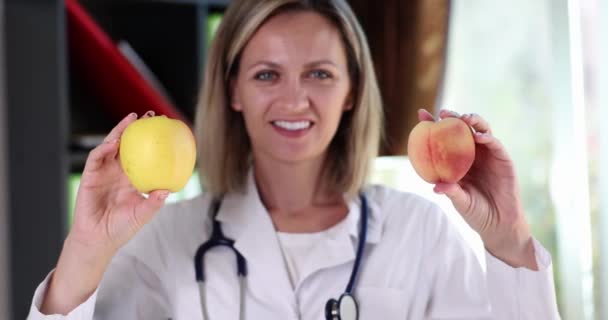 Un médecin nutritionniste souriant tient des pommes et des fruits de la pêche. Saveur de fruit bienfaits pour la santé et vitamines - Séquence, vidéo