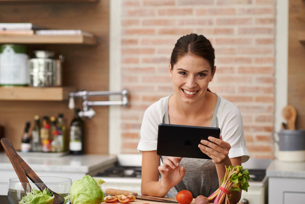 I can store thousands of recipes on my tablet. Portrait of an attractive young woman using her tablet in the kitchen - Foto, Imagem