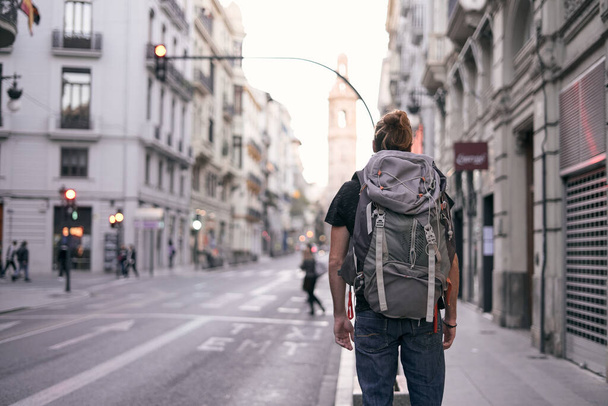 νεαρός καυκάσιος άνδρας στέκεται με την πλάτη του σε ένα δρόμο της πόλης με ένα μεγάλο σακίδιο στην πλάτη του, valencia, Ισπανία - Backpacker ταξιδιωτική έννοια - Φωτογραφία, εικόνα