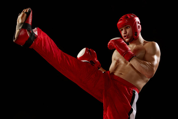 Champion. Studio shot of male kickboxer, mma fighter in motion and action isolated over dark background. Muay thai. Sport, competition, energy, combat sports. Red and black - Foto, afbeelding