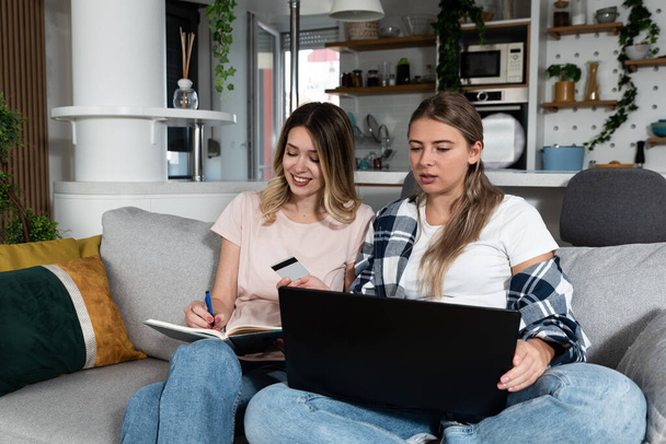 Two women, roommates and business partners, jot down and steal business ideas from the internet about what they can do with their bank credit card and start their own online company. - Fotoğraf, Görsel