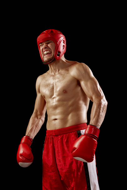 Champion. Studio shot of male kickboxer, mma fighter in motion and action isolated over dark background. Muay thai. Sport, competition, energy, combat sports. Red and black - Φωτογραφία, εικόνα