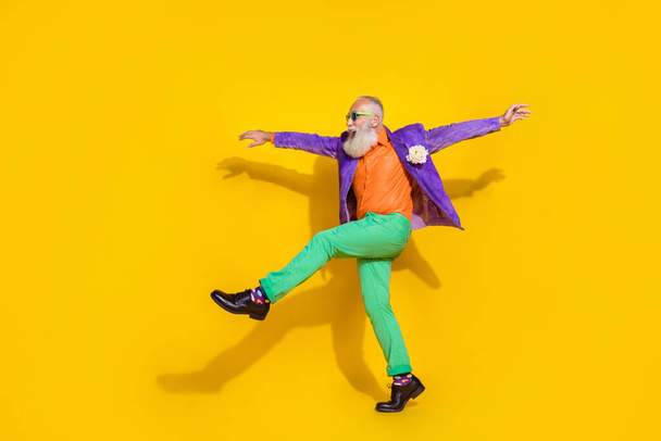 Full length photo of positive funky man wear purple velvet jacket walking hands sides discotheque isolated yellow color background. - Foto, afbeelding
