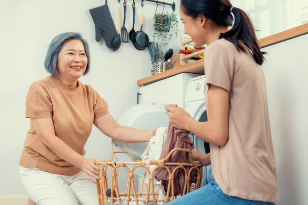 Daughter and mother working together to complete their household chores near the washing machine in a happy and contented manner. Mother and daughter doing the usual tasks in the house. - Photo, Image
