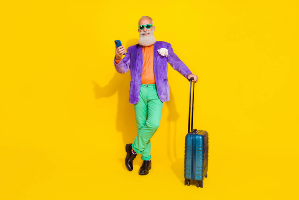 Full length portrait of positive grandfather hold use telephone suitcase isolated on yellow color background. - Фото, зображення