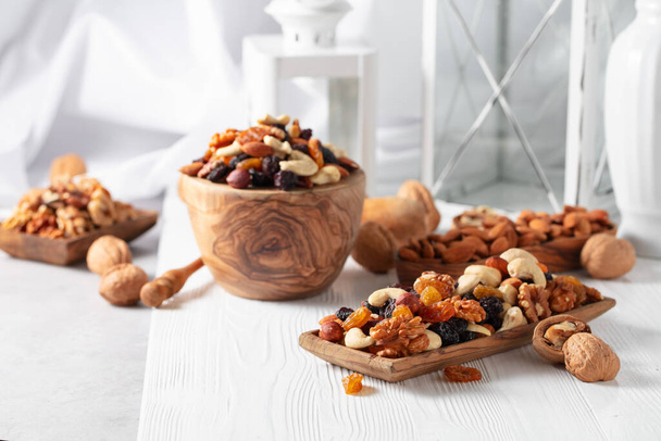 Sekoita pähkinöitä ja rusinoita valkoisella puupöydällä. Esitetyt rusinat, saksanpähkinät, hasselpähkinät, cashew, pekaanipähkinät ja mantelit. - Valokuva, kuva